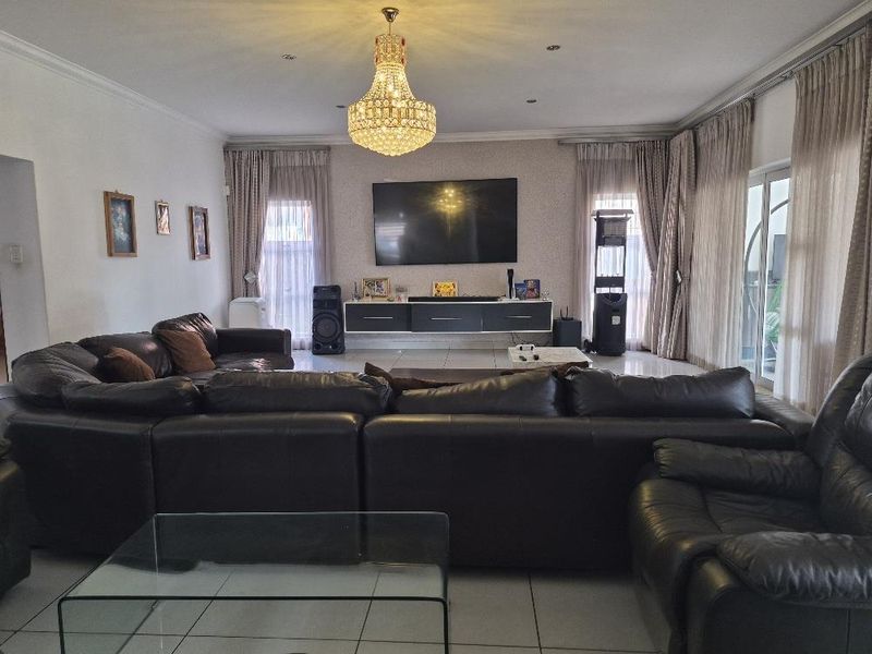 Spacious living room featuring tiled flooring, a central crystal chandelier, recessed lighting, and a wall-mounted floating media console with access to an outdoor area.