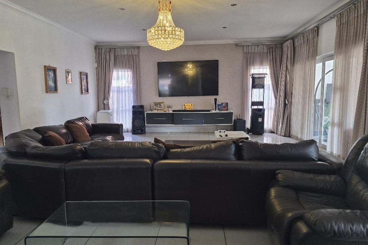 Spacious living room featuring tiled flooring, a central crystal chandelier, recessed lighting, and a wall-mounted floating media console with access to an outdoor area.