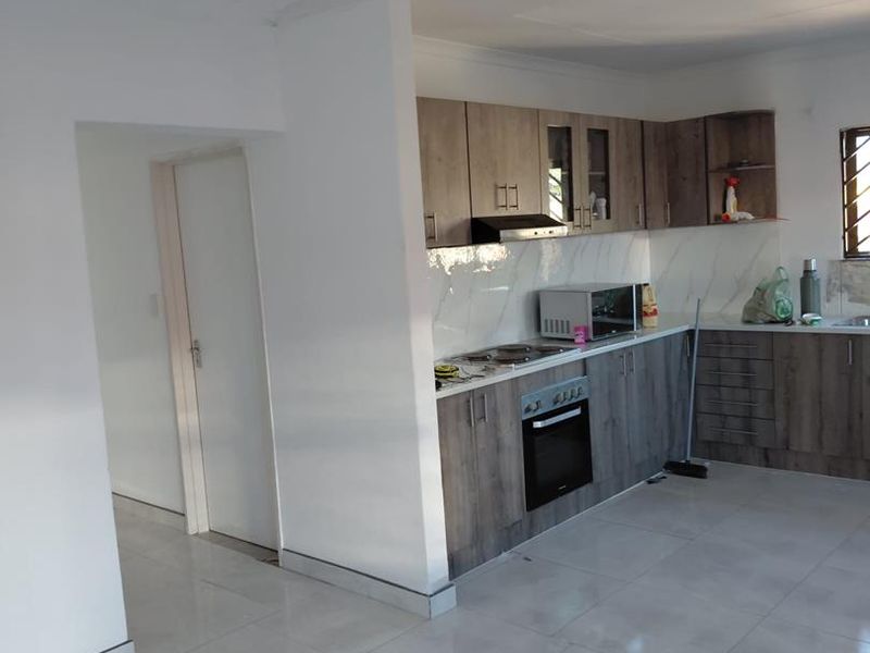 Modern kitchen featuring wood-grain cabinetry, marble-look splashback, built-in oven, extractor fan, and light-colored ceramic floor tiles.