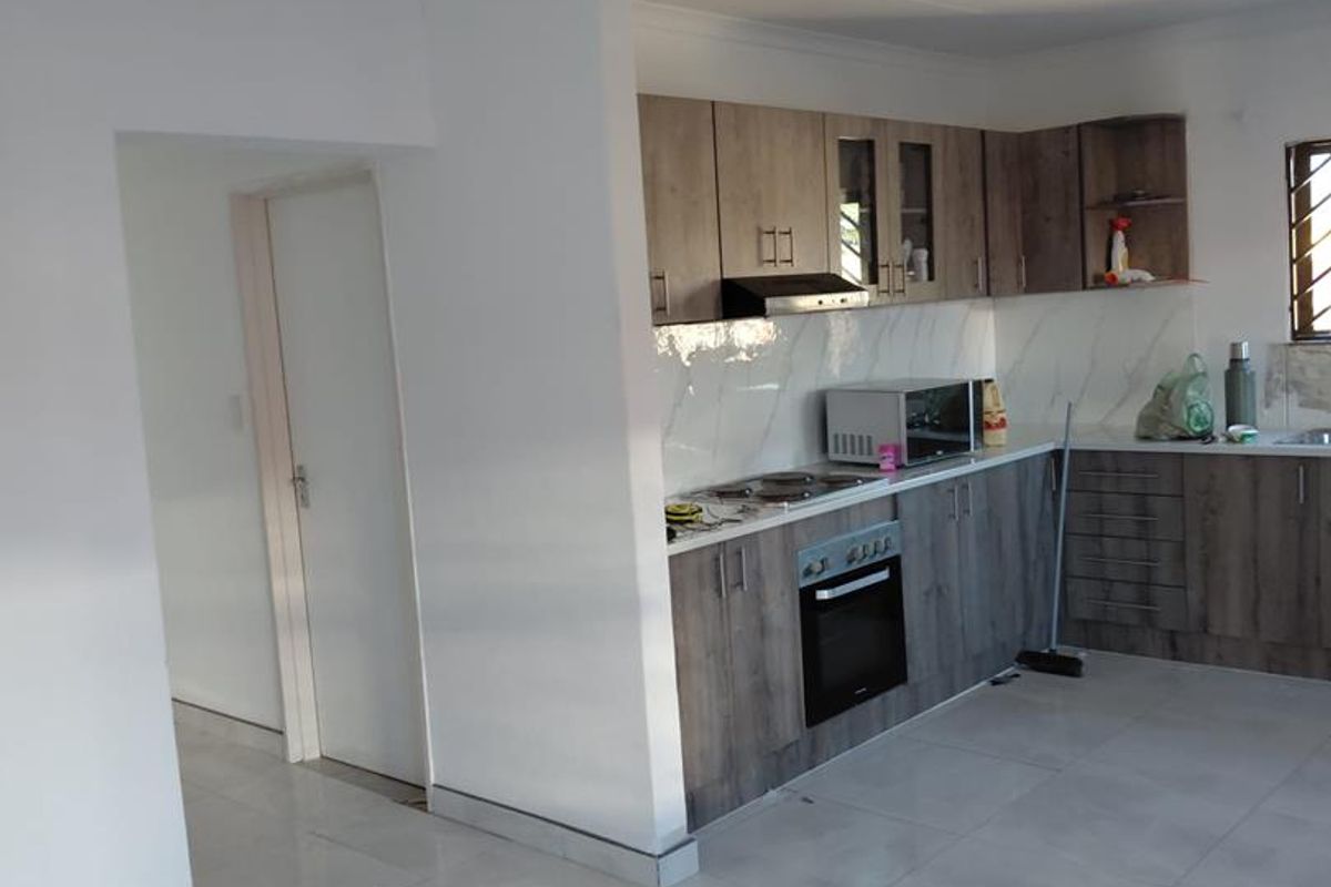 Modern kitchen featuring wood-grain cabinetry, marble-look splashback, built-in oven, extractor fan, and light-colored ceramic floor tiles.