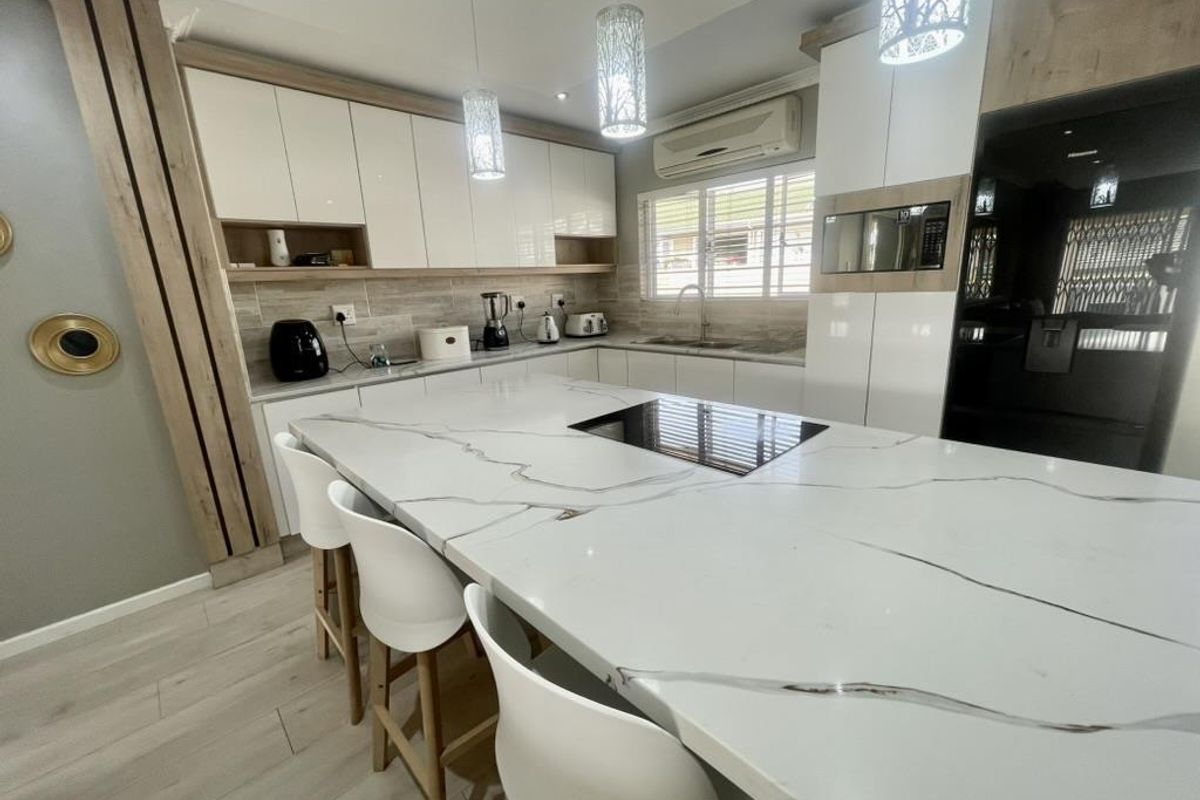 Modern kitchen featuring a large stone-topped island, high-gloss cabinetry, integrated appliances, and contemporary lighting, offering a sleek and functional culinary space.