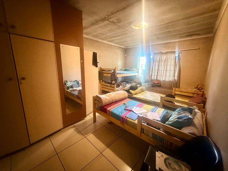 A bedroom featuring built-in cupboards and tiled flooring, currently requiring maintenance and cosmetic updates to the ceiling and wall finishes.