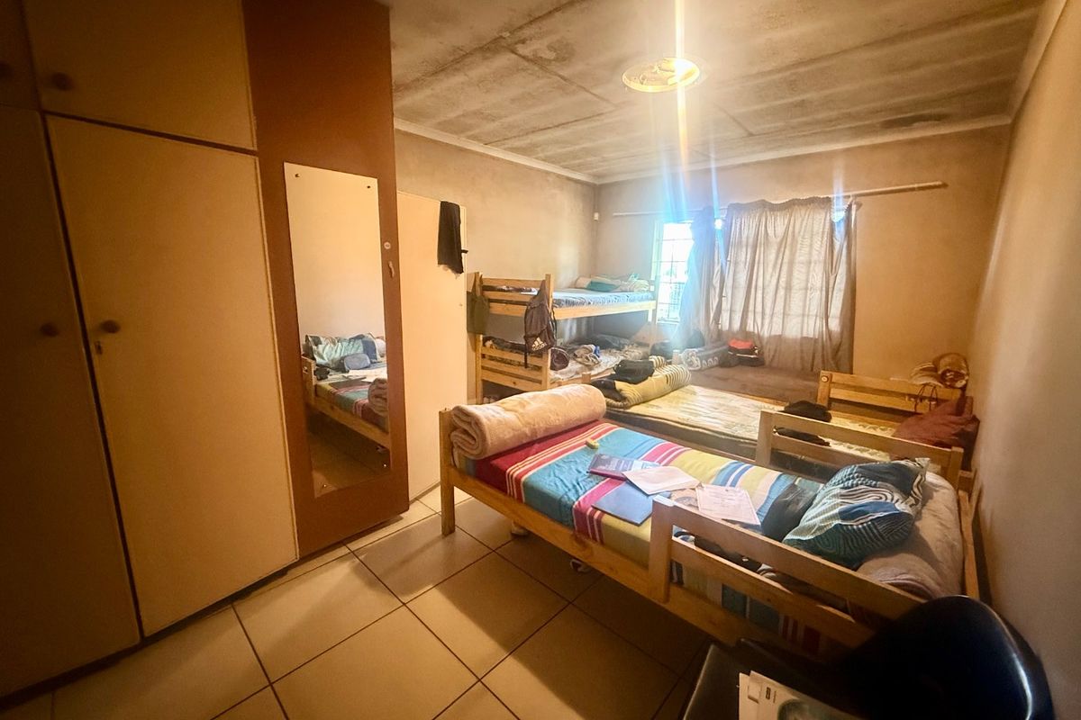 A bedroom featuring built-in cupboards and tiled flooring, currently requiring maintenance and cosmetic updates to the ceiling and wall finishes.