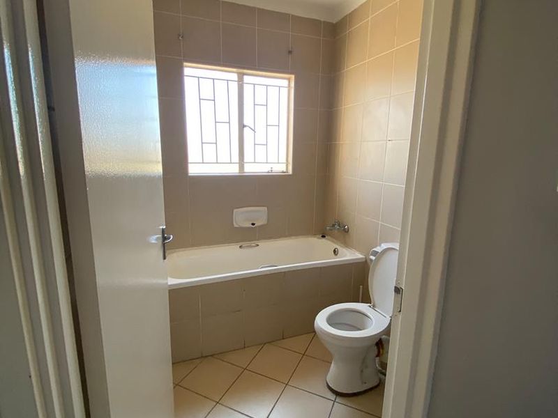 A functional bathroom featuring a built-in bathtub, toilet, and neutral tiled finishes, offering a clean and simple layout.