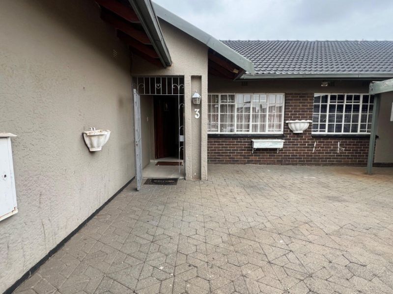Front entrance area featuring a paved driveway, brick and rendered facade, security gate, and tiled roof.