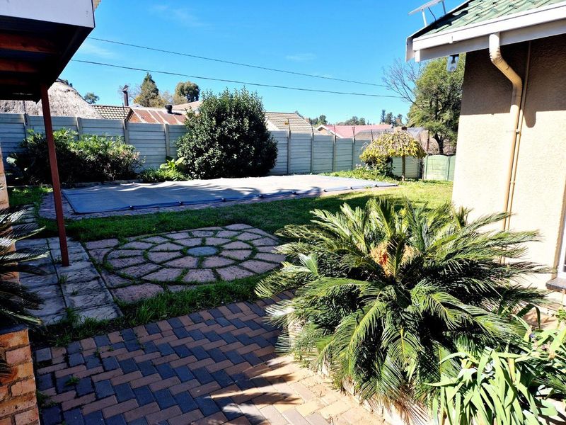 Rear garden area featuring a swimming pool with a cover, paved patio space, and established boundary walling.