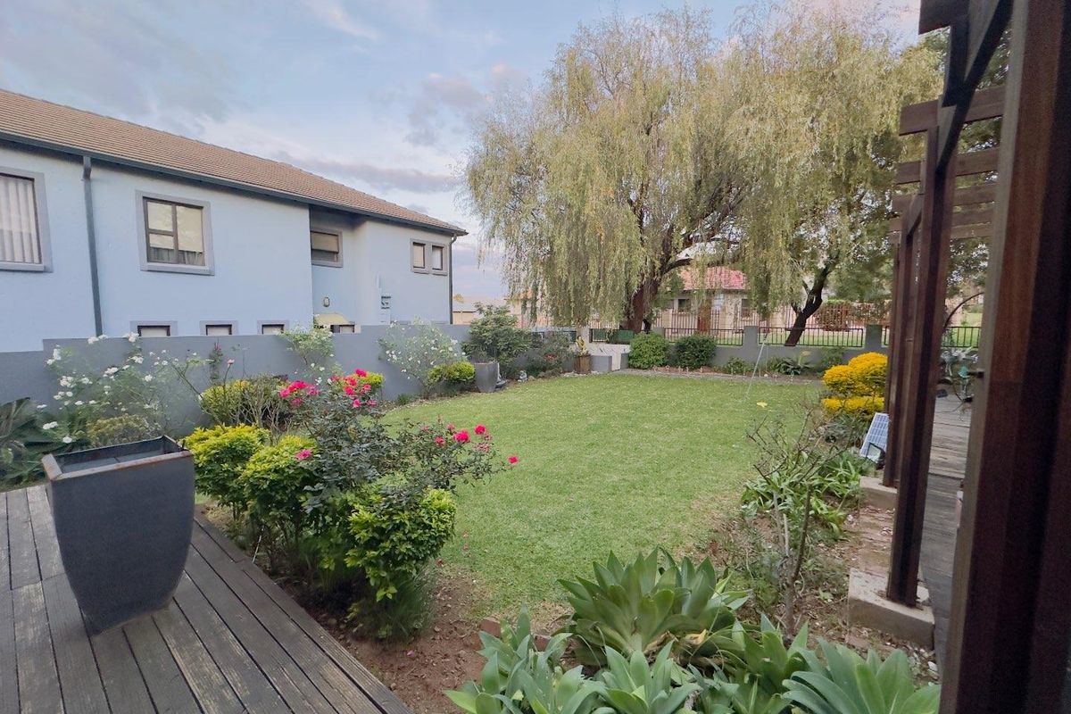 A well-maintained rear garden featuring a timber deck, manicured lawn, established perimeter landscaping, and a boundary wall.
