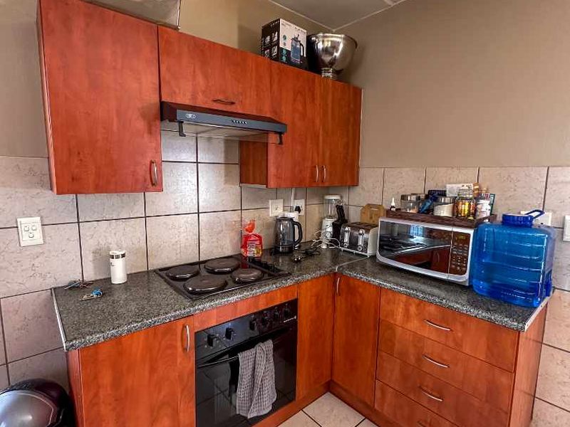 Compact kitchen featuring cherry-toned cabinetry, granite countertops, built-in oven, electric hob, and ceramic tile finishes.