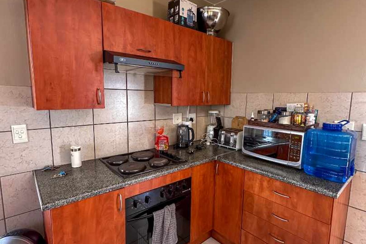 Compact kitchen featuring cherry-toned cabinetry, granite countertops, built-in oven, electric hob, and ceramic tile finishes.