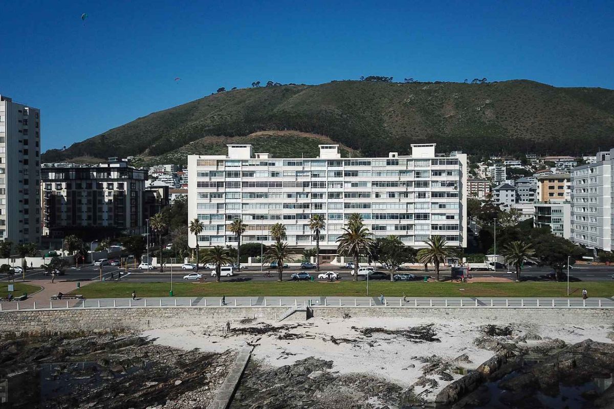 Aerial view of a multi-story apartment building situated along the coastline, featuring a prominent facade with numerous balconies and proximity to the beach.