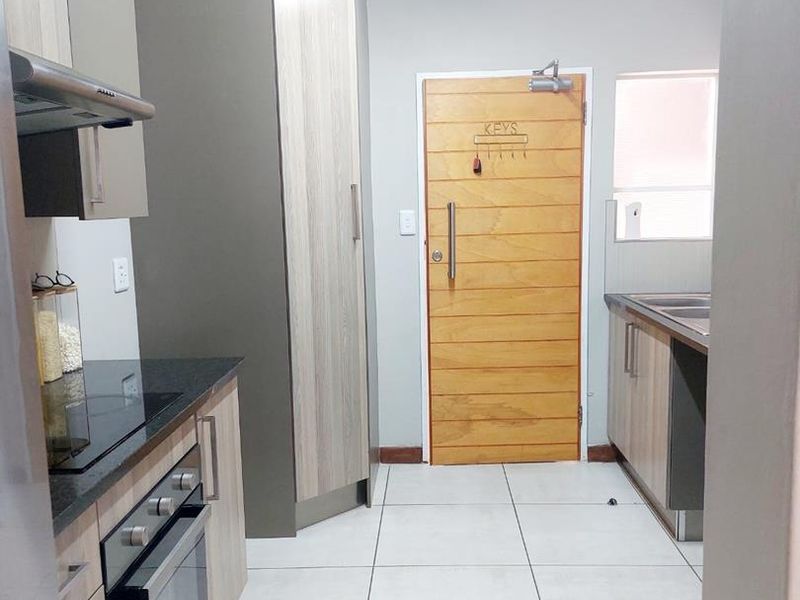 A clean, modern kitchen featuring built-in cabinetry, an electric hob with extractor, built-in oven, double sink, and neutral tiled flooring.