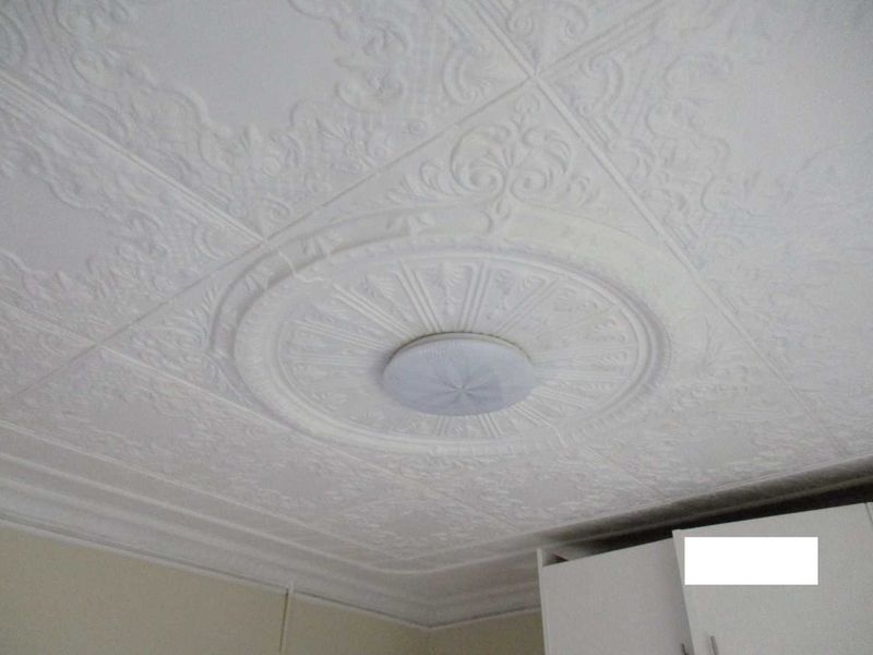 A close-up view of an interior ceiling featuring decorative embossed tiles, a central ceiling rose, and a flush mount light fixture.