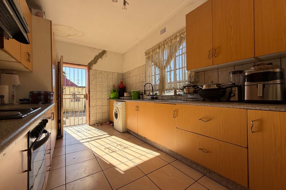 Functional kitchen featuring wood-look cabinetry, tiled flooring, and direct access to the exterior. The space requires cosmetic updates to address wall and ceiling damage.