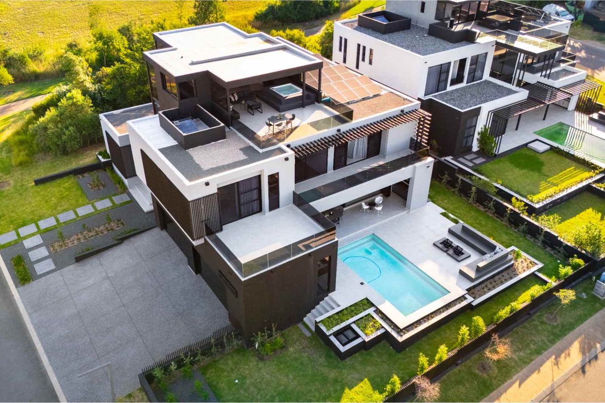 Aerial view of a modern multi-story residential property featuring a swimming pool, rooftop terrace with spa, solar panels, and landscaped garden areas.