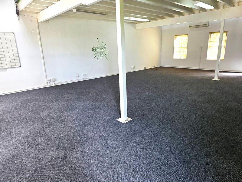 Spacious open-plan office area featuring exposed ceiling beams, carpeted flooring, and wall-mounted air conditioning, providing a versatile workspace environment.