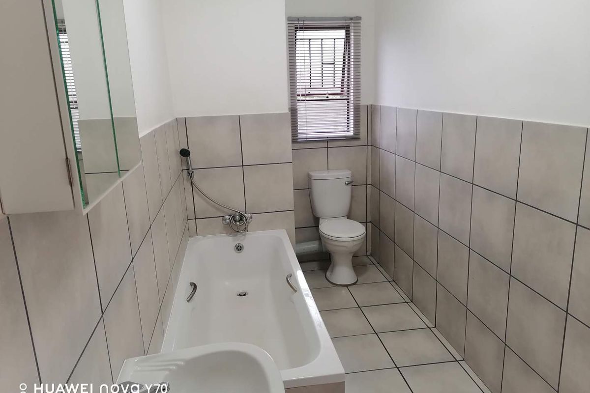 A functional bathroom featuring a bathtub, toilet, and tiled finishes, providing a clean and neutral space ready for personalization.