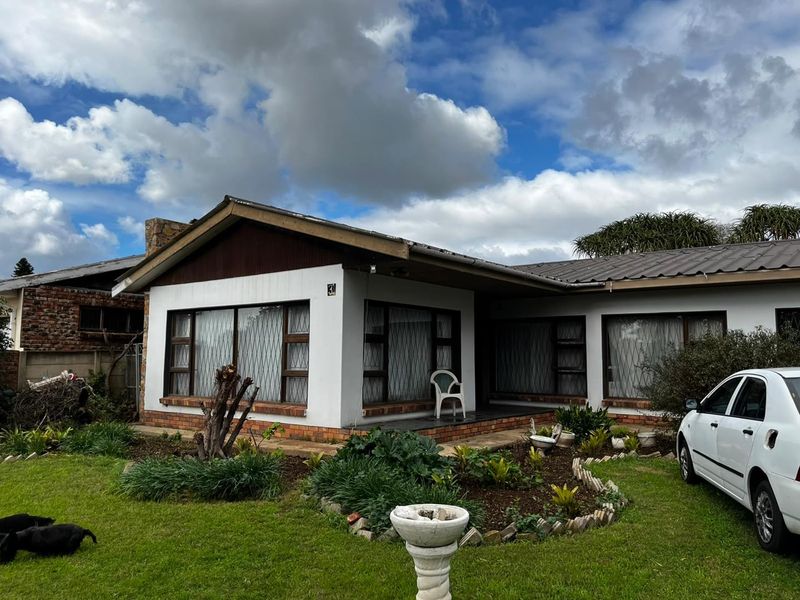 Front elevation of a cottage featuring a metal roof, stone chimney, and a covered porch area with security-barred windows.