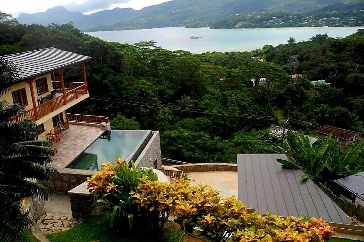 Elevated view of a villa featuring an infinity pool, multi-level balconies, and expansive tropical landscape overlooking the bay.