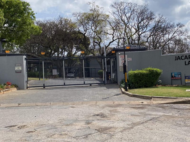 Front entrance view of Jacaranda Lane apartment complex featuring a secure gated access point, perimeter wall, and paved driveway.