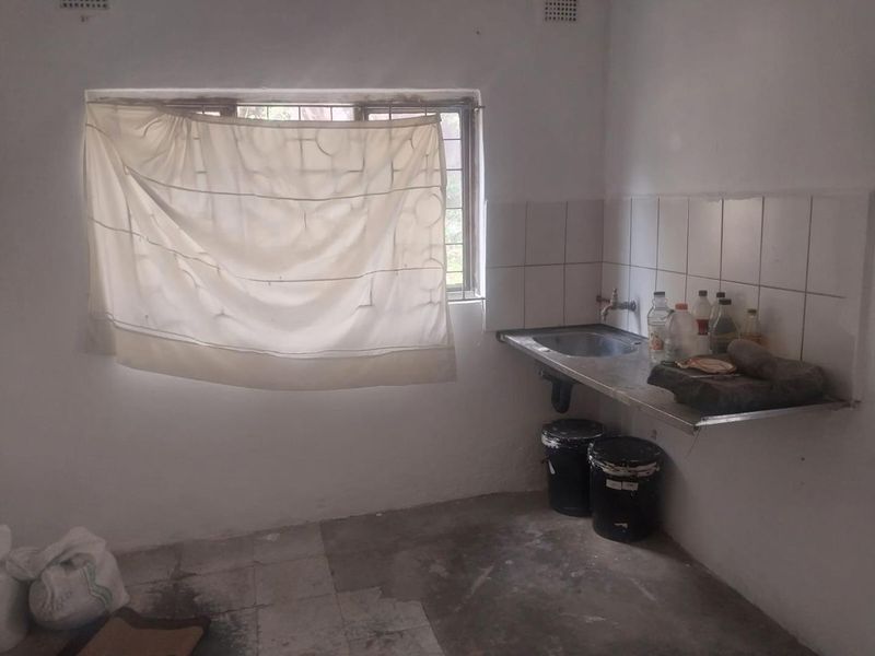 A basic scullery or utility area featuring a stainless steel sink, tiled splashback, and security bars on the window.