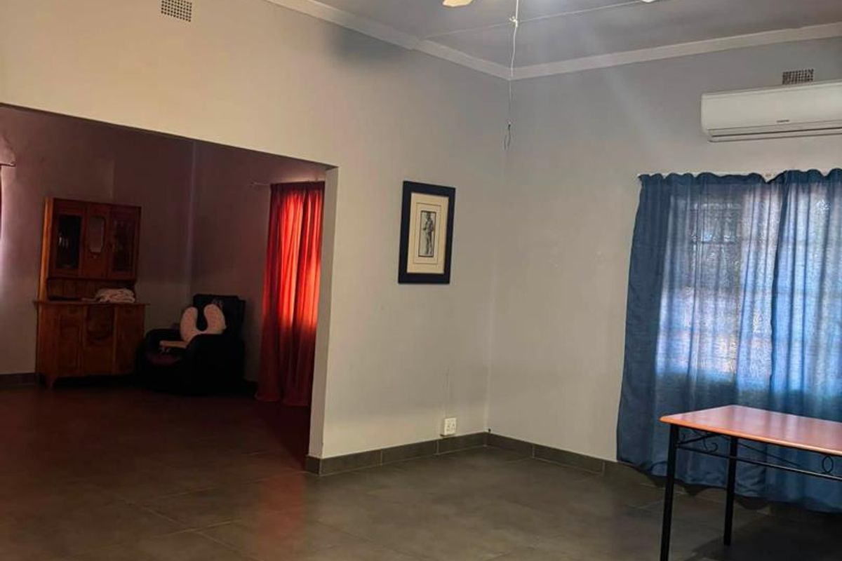 Spacious living area featuring tiled flooring, a ceiling fan, and a wall-mounted air conditioning unit, with an open-plan flow to an adjacent room.