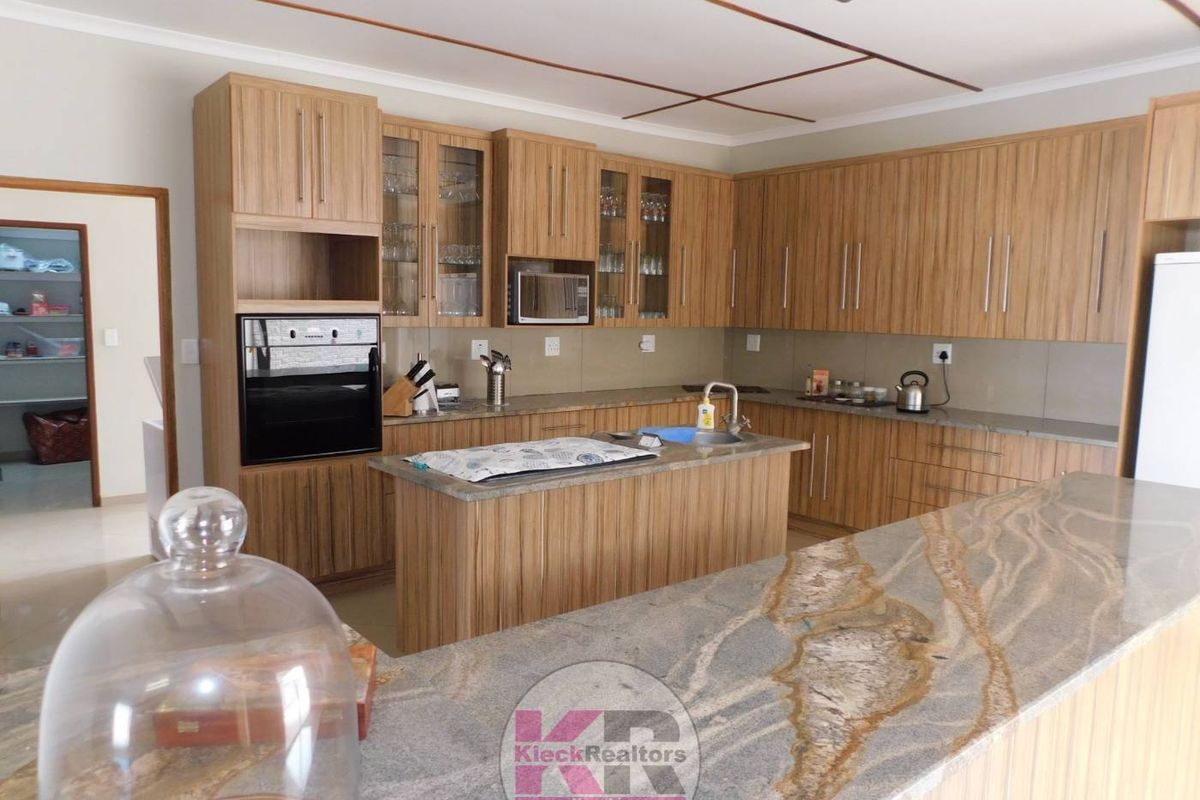 Spacious kitchen featuring extensive wood-finish cabinetry, granite countertops, a central island, and integrated appliances, with an adjacent scullery area.
