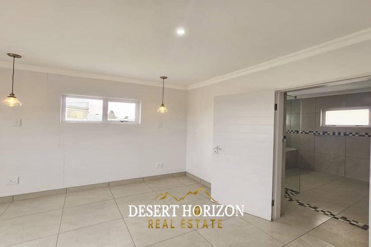 A bright, neutral bedroom featuring tiled flooring, recessed lighting, and an en-suite bathroom with a glass shower enclosure.