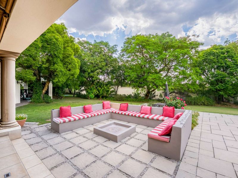 A spacious covered patio featuring built-in concrete seating and a central fire pit, overlooking a lush, well-maintained garden.