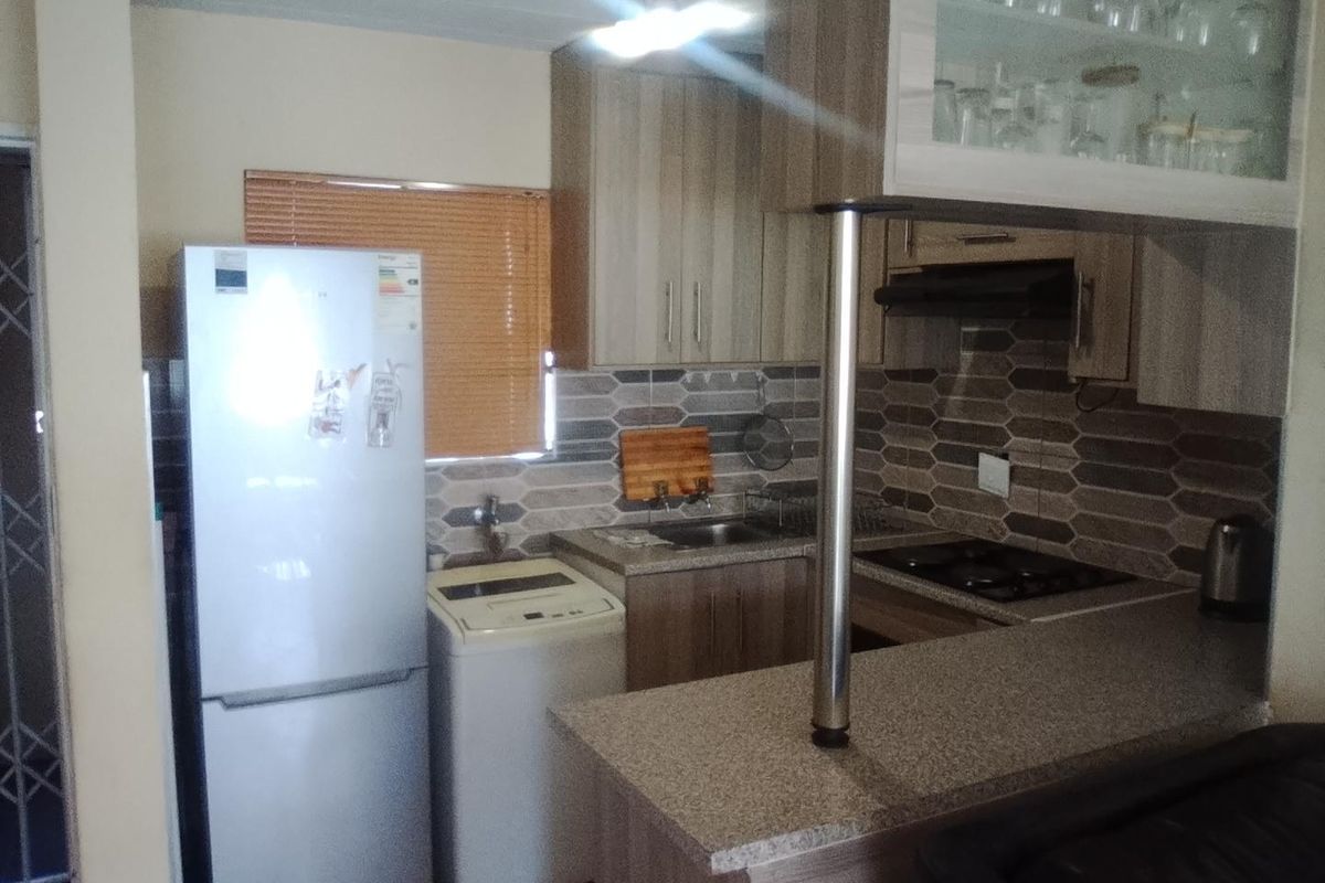Compact kitchen featuring modern cabinetry, stone-look countertops, a tiled backsplash, and a breakfast bar, providing a functional and efficient cooking space.