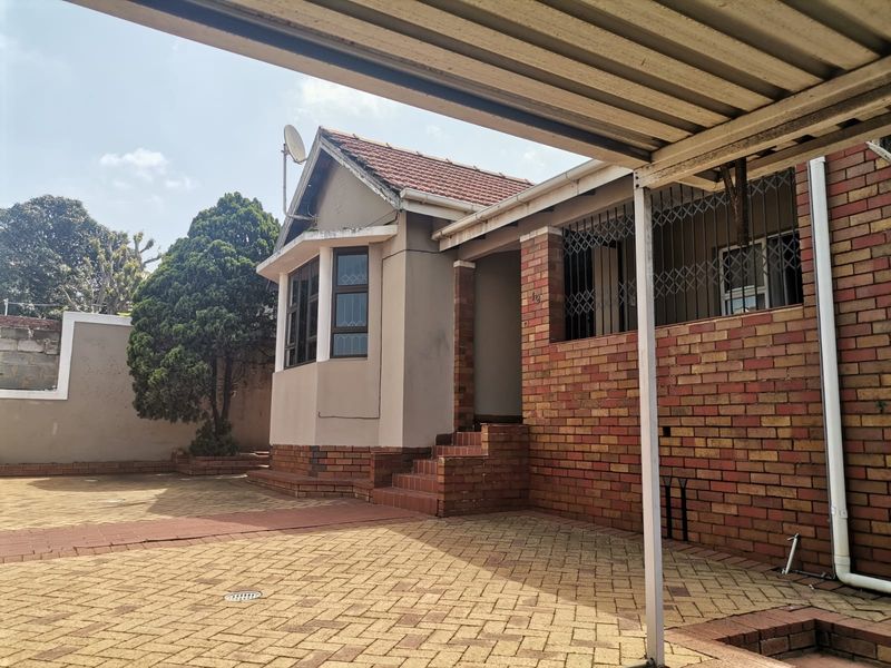 Front exterior view of the house featuring a brick facade, tiled roof, paved driveway, and a covered carport area.