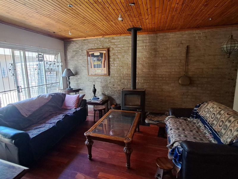 Cozy living room featuring a wood-burning fireplace, exposed brick wall, timber ceiling, and sliding glass doors leading to the exterior.