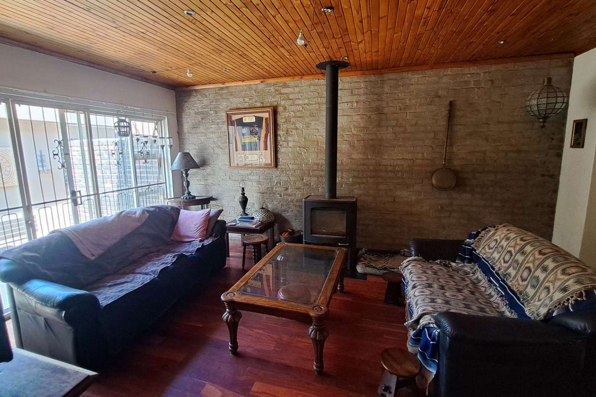 Cozy living room featuring a wood-burning fireplace, exposed brick wall, timber ceiling, and sliding glass doors leading to the exterior.