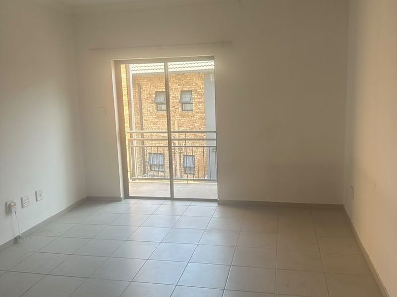 A bright, empty living area featuring neutral tiled flooring and a sliding glass door that provides access to a private balcony.