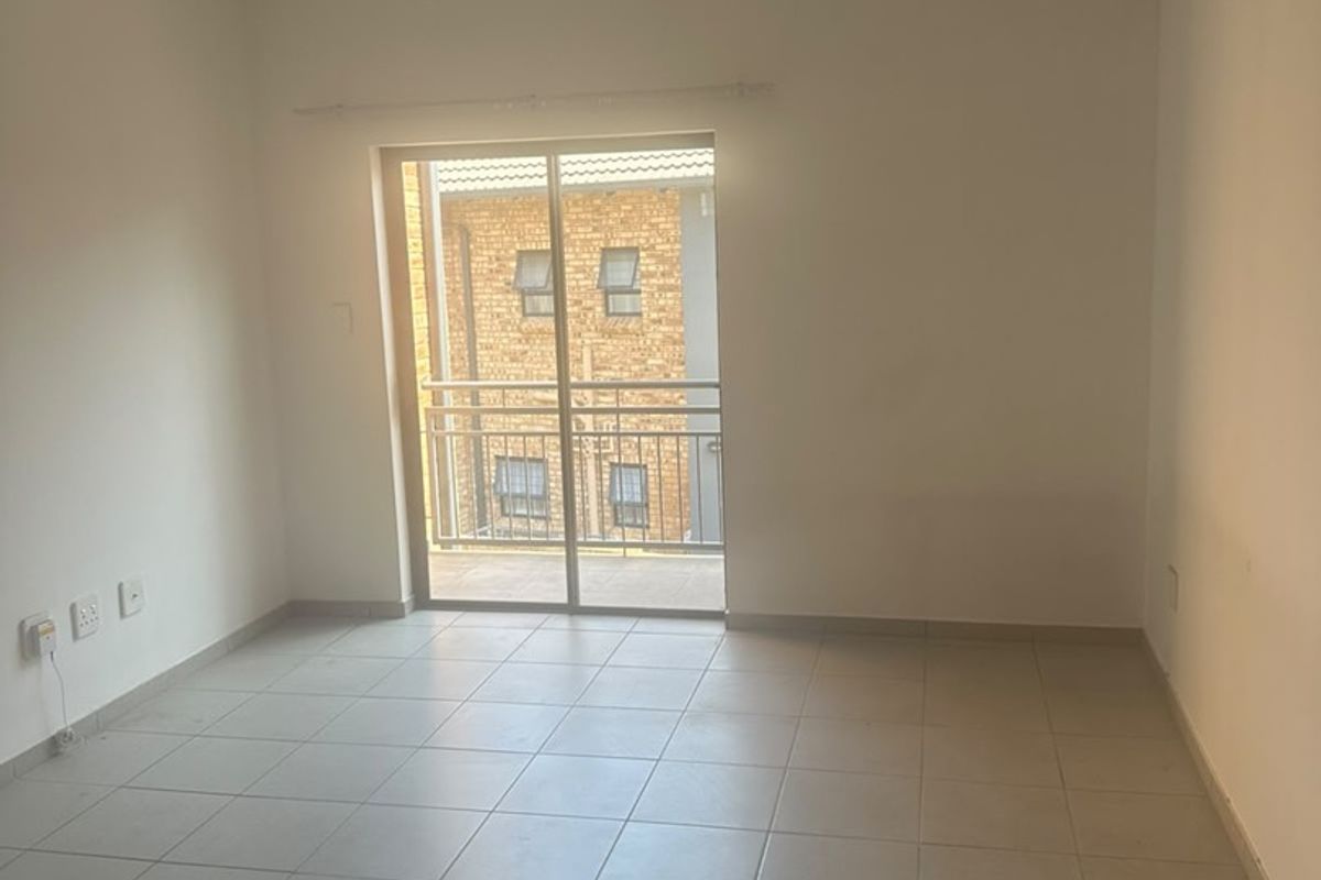 A bright, empty living area featuring neutral tiled flooring and a sliding glass door that provides access to a private balcony.