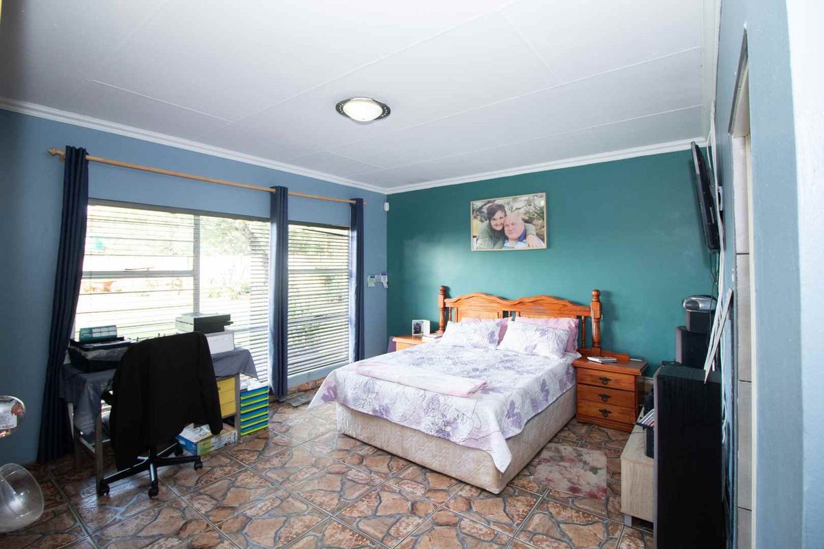 Spacious bedroom featuring large windows, tiled flooring, and a feature wall, offering a functional layout with ample natural light.