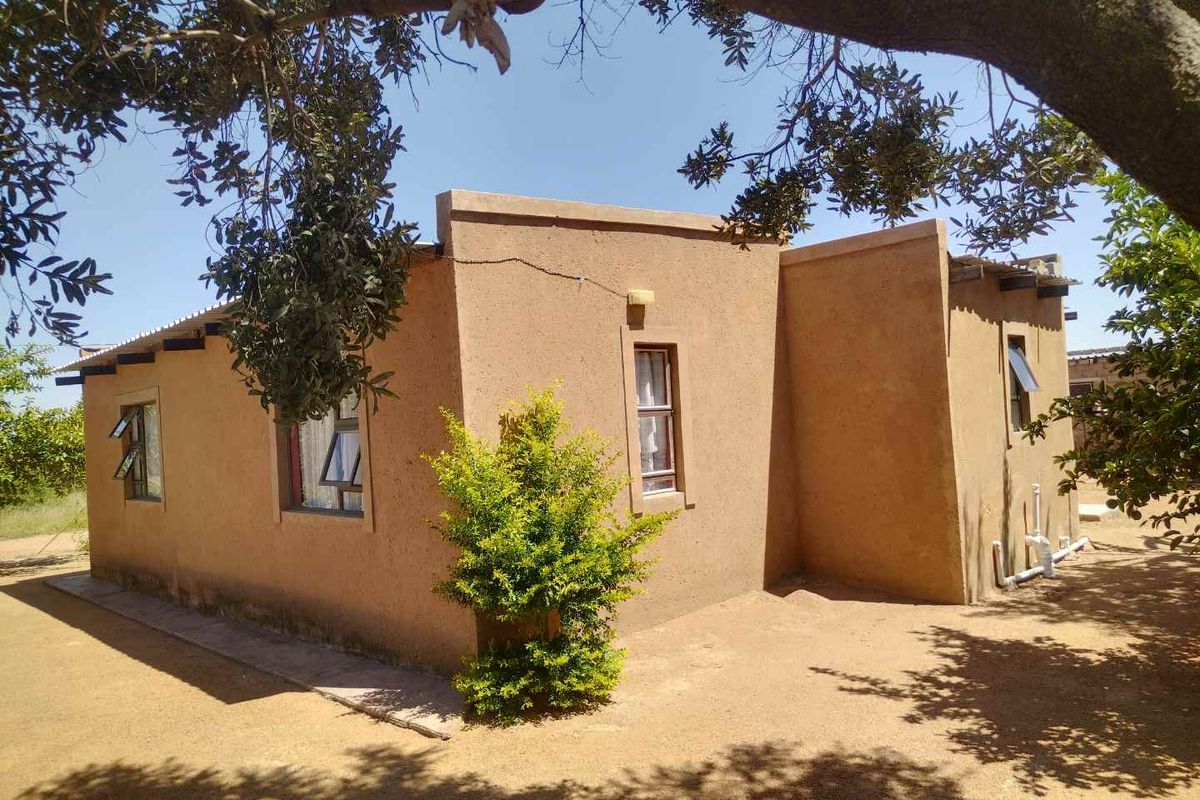 Exterior view of a single-story house featuring a textured render finish, metal window frames, and a simple architectural design set in a natural landscape.