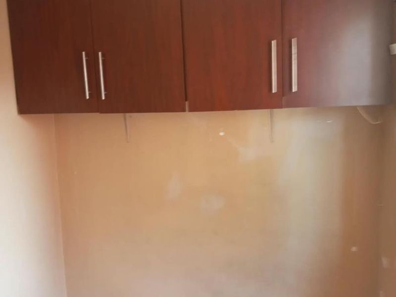 A small utility or laundry area featuring wall-mounted wooden cabinetry, requiring cosmetic updates to the wall finishes.