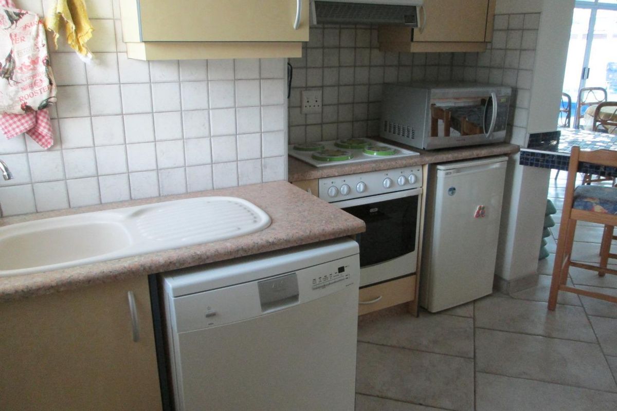A compact kitchen featuring laminate countertops, built-in oven with hob, extractor fan, and tiled flooring, offering a functional layout for daily meal preparation.