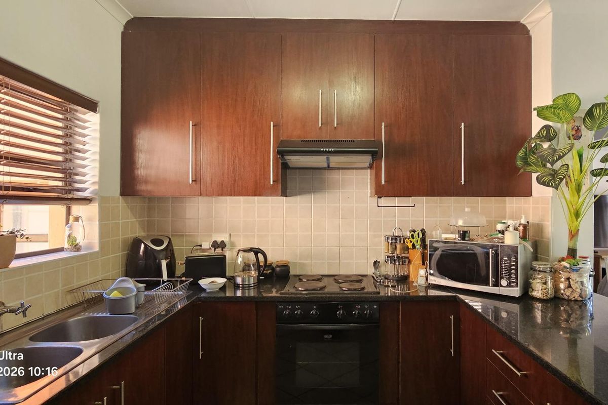A functional kitchen featuring dark wood cabinetry, granite countertops, a built-in oven with hob, and a tiled backsplash with a double sink.