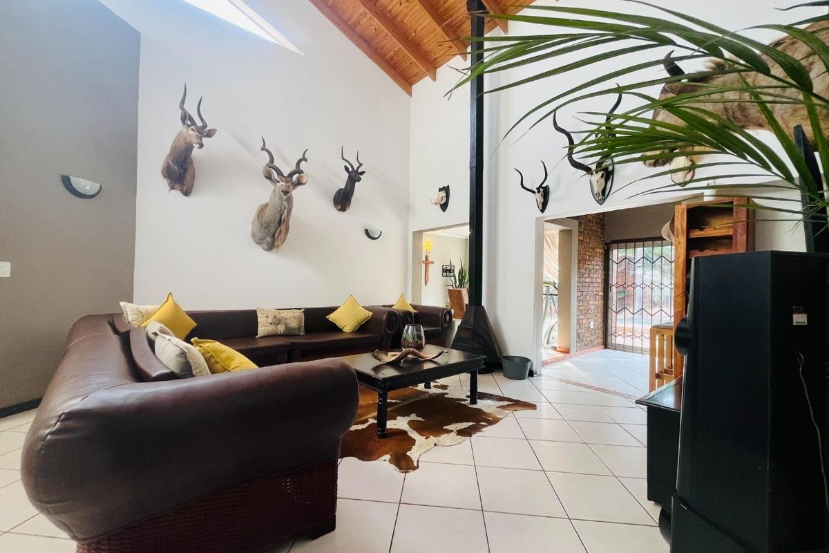 Spacious living room featuring high vaulted timber ceilings, tiled flooring, and a prominent black metal fireplace, leading to an adjacent entryway.