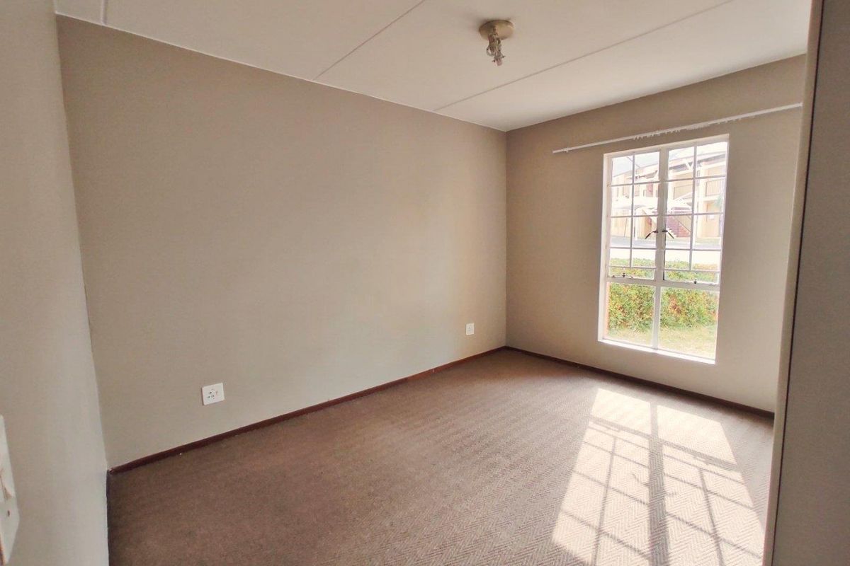 A clean, empty bedroom featuring neutral wall tones, carpeted flooring, and a window with security bars, offering a blank canvas for personalization.