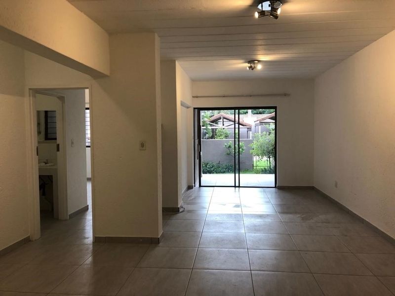 Spacious, empty living area featuring neutral tiled flooring, exposed beam ceilings, and a sliding glass door providing access to the outdoor space.