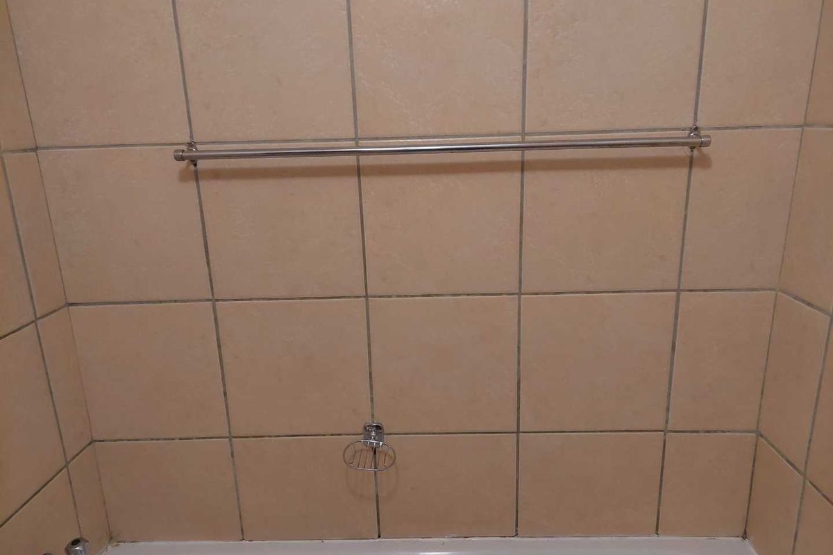 A bathroom shower area featuring beige wall tiles, a metal towel rail, a soap dish, and a bathtub with a faucet.