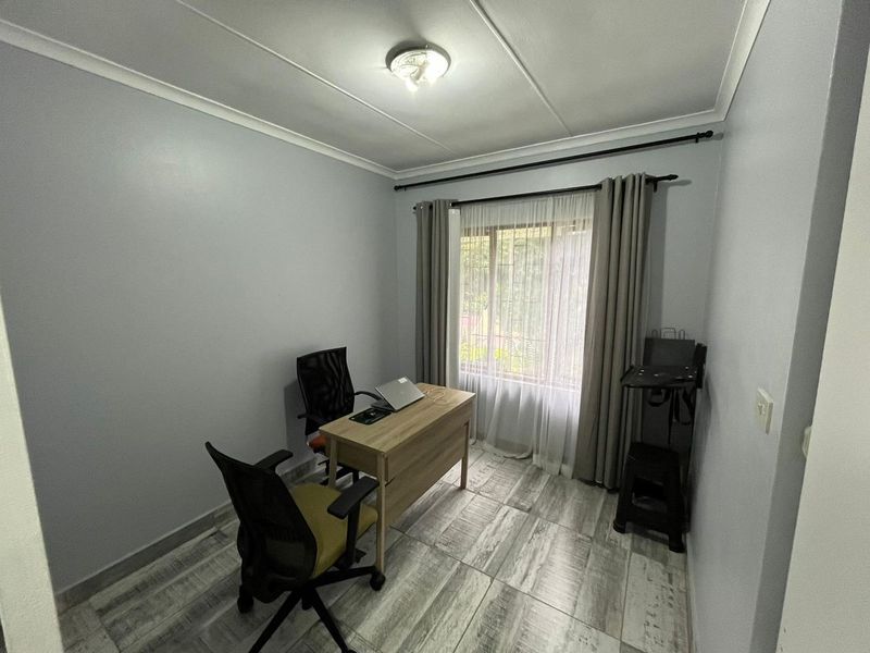 A functional home office space featuring tiled flooring, neutral wall tones, and a window providing natural light.