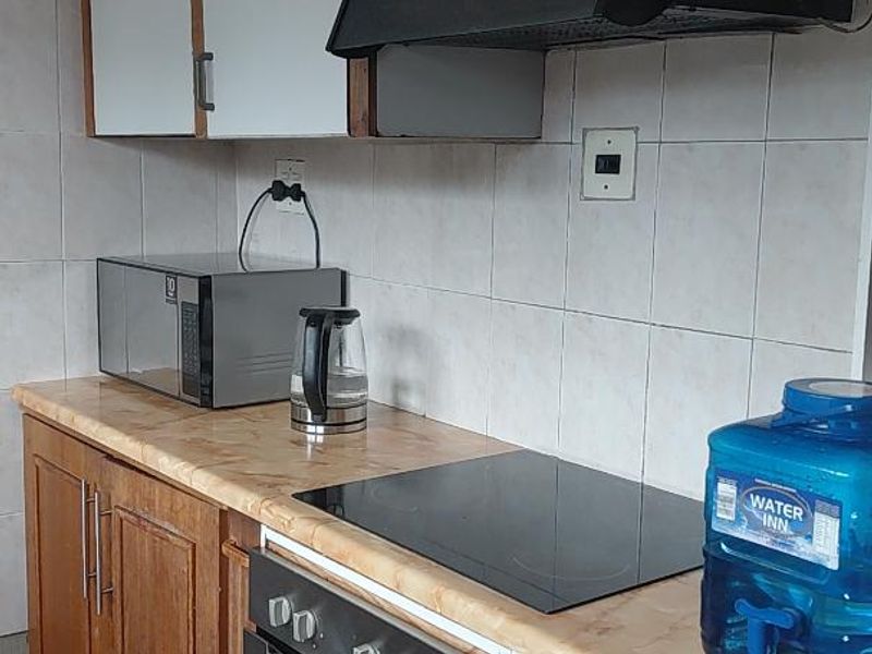 A functional kitchen featuring wooden cabinetry, a laminate countertop, built-in oven, and electric hob with a tiled backsplash.