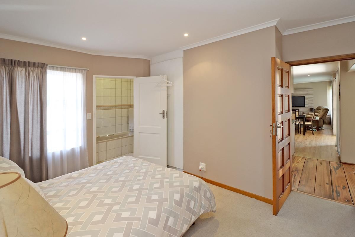 A well-maintained bedroom featuring neutral wall tones, carpeted flooring, and an en-suite bathroom, with direct access to the adjacent living area.