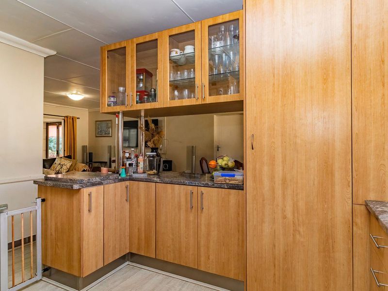 A functional kitchen featuring light wood-finish cabinetry, laminate countertops, and a mirrored backsplash, offering ample storage space with a full-height pantry unit.