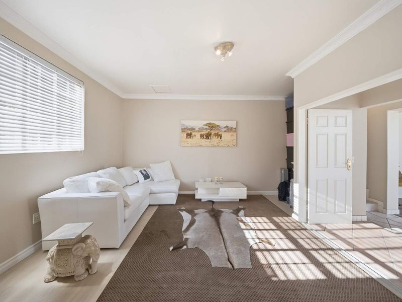 A bright and well-maintained living room featuring crown molding, neutral wall finishes, and large windows with fitted venetian blinds.