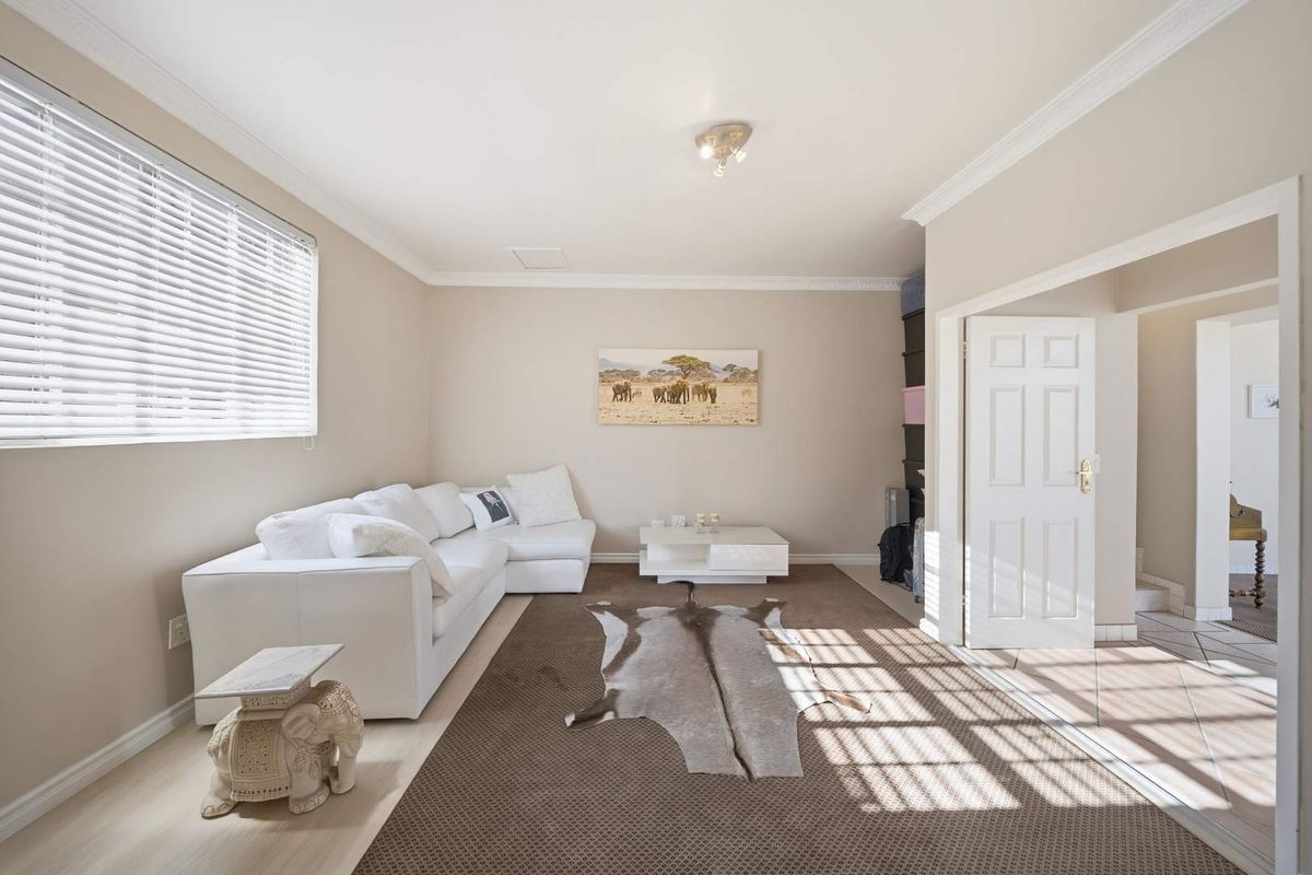 A bright and well-maintained living room featuring crown molding, neutral wall finishes, and large windows with fitted venetian blinds.