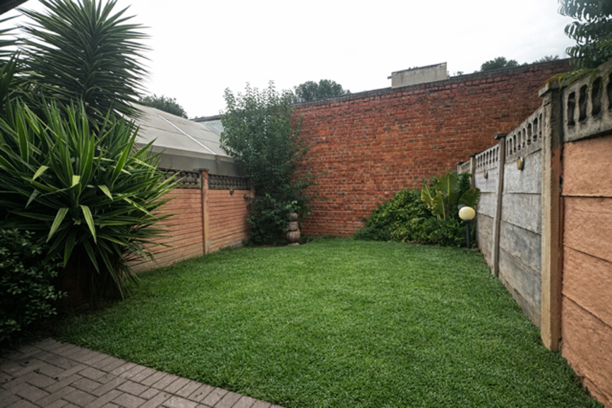 A private rear garden featuring a lawn area, paved patio section, and high perimeter brick and concrete boundary walls.